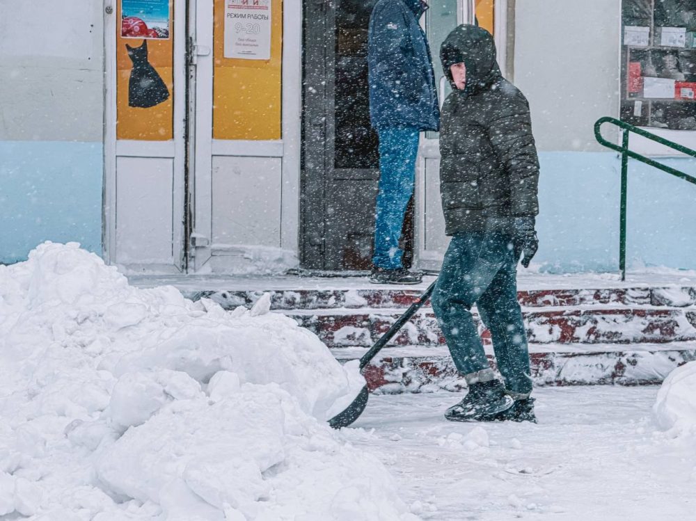мужчина убирает снег в метель